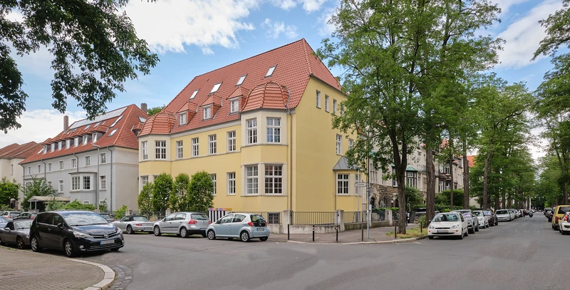 Gelbes mehrst&ouml;ckiges Eckgeb&auml;ude in einer Wohnstra&szlig;e mit Parkpl&auml;tzen und B&auml;umen &ndash; Au&szlig;enaufnahme der Oberberg Tagesklinik Hannover